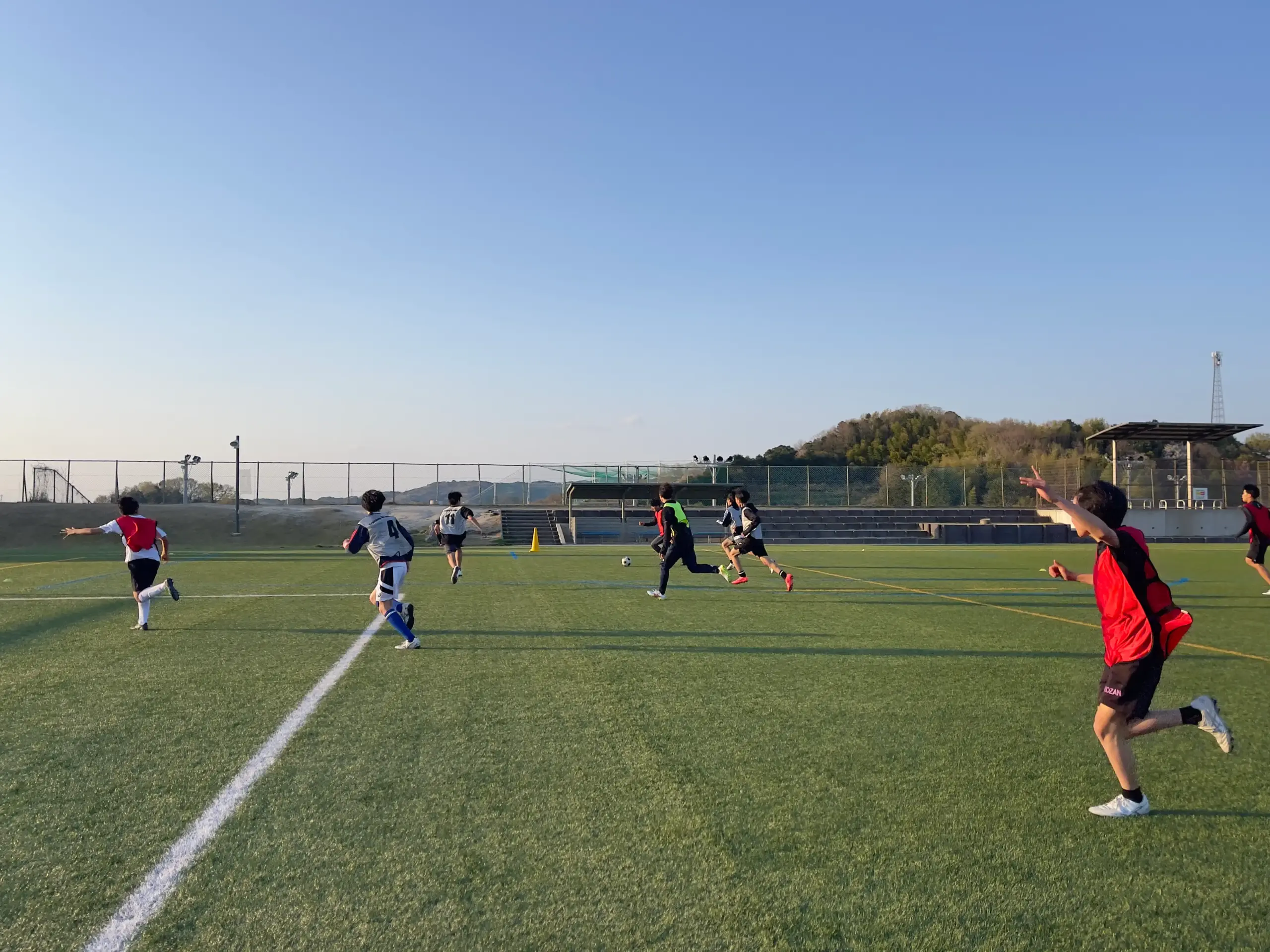 緑の人工芝グラウンドでサッカーの練習をする中学生たち